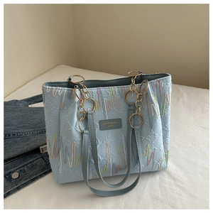Close-up of light blue tote bag featuring colorful embroidery and logo metal plaque