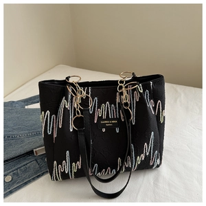 Detailed view of black embroidery tote bag with wave patterns and golden metal hardware
