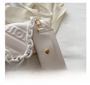 Close-up of cream PU leather charm with gold snap button and chain on quilted handbag