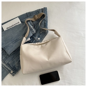 Minimalist beige nylon tote bag on a white fabric background with casual accessories