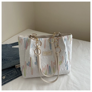 Detailed view of the wave-patterned stitching and golden chain on the cream tote bag