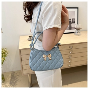 Détail du sac à main matelassé bleu clair avec boucle nœud doré porté à l'épaule