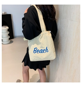 Detail of a beige drawstring tote bag with blue Beach lettering and wide shoulder strap