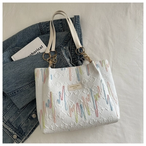 Macro detail of a white tote bag featuring colorful wavy embroidery and gold chain straps.