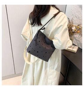 Detail of black shoulder bag with laser-cut star patterns worn by a model in a modern room