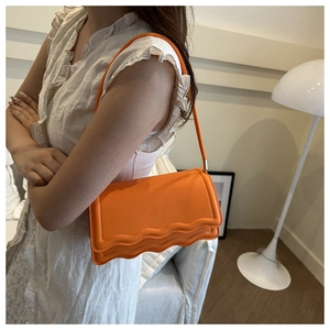 Close-up of bright orange crossbody bag featuring unique scalloped edge detail and leather texture