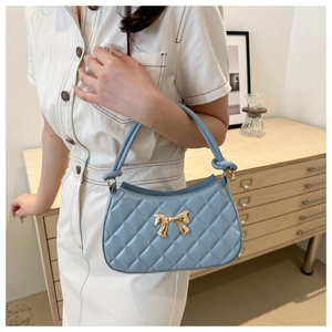 Détail d'un sac à main matelassé bleu clair avec boucle dorée et poignée à nœuds décoratifs