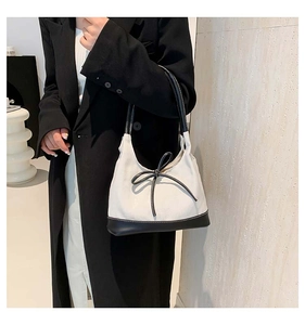 Detail of canvas tote with black leather trim and bow on a model in a black blazer
