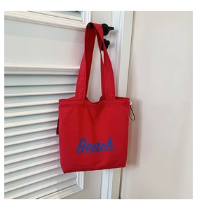 Detail of red canvas tote bag featuring blue Beach lettering and side drawstring cord
