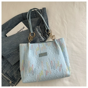 Detail of light blue tote bag with quilted texture, embroidery and gold chain strap