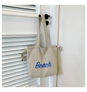 Detail of light khaki tote bag with blue Beach text and adjustable drawstring side