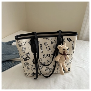 Detail of graffiti print tote bag in cream white featuring a black teddy bear charm