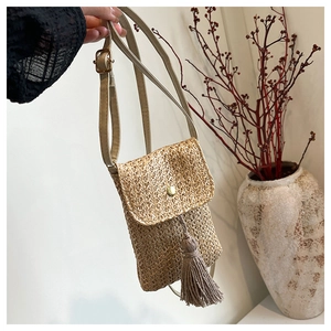 Detail of a straw woven crossbody phone bag with gold metal buckle and long tassel charm
