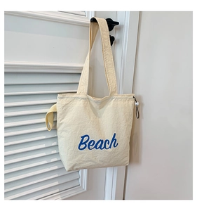 Detail of off-white canvas tote bag featuring blue Beach lettering and drawstring closure