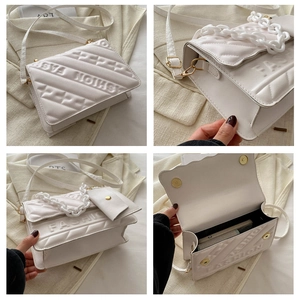 Detail of white quilted crossbody bag with embossed lettering and chunky chain strap