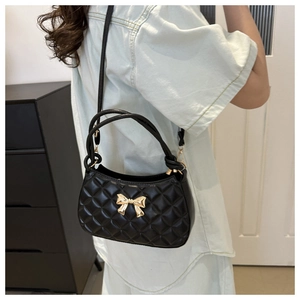 Gros plan du sac matelassé noir avec nœud doré et bandoulière en cuir véritable