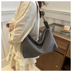 Detail of a large dark grey nylon crescent bag worn over a beige lace dress