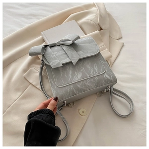 Detail of light gray backpack featuring a large bow and marble textured leather