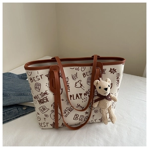 Detail view of large printed tote bag with graffiti pattern and cute bear charm attachment