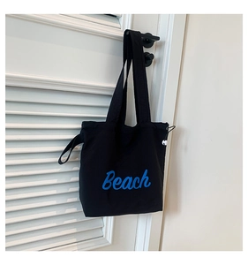 Detail of black canvas tote bag showing blue Beach print and side drawstring closure