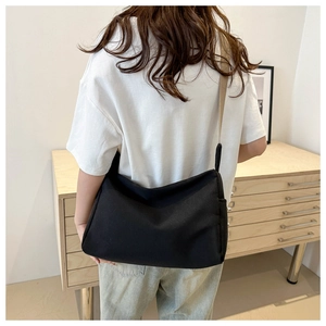 Back view of a black nylon crossbody bag with adjustable beige strap on a model