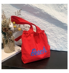 Detail of red canvas tote bag featuring blue Beach lettering and drawstring closure