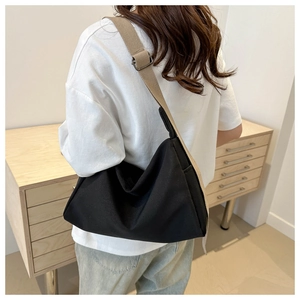 Detail view of large black nylon tote bag with wide beige adjustable strap on model