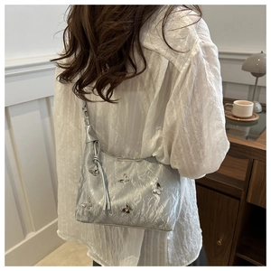 Sac à bandoulière argenté avec texture plissée et détails papillon portés par le modèle