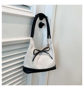 Detail of canvas bucket bag with contrast leather trim and decorative bow accent