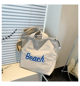 Detailed view of beige nylon tote bag with blue Beach lettering and side drawstring