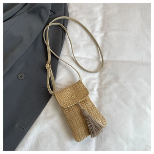 Detail of straw woven phone bag featuring tassel fringe and gold metal snap button closure