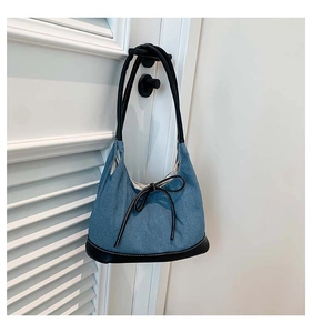 Detail of blue denim bucket bag with black leather base and decorative ribbon bow
