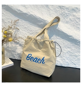 Detail of beige nylon drawstring tote bag with blue Beach text and cord lock buckle