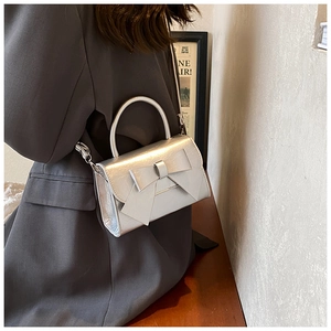 Petit sac argenté métallisé avec nœud décoratif, porté à l'épaule avec sa bandoulière