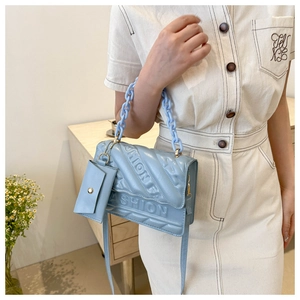 Detail of light blue quilted crossbody bag featuring embossed fashion logo and chain strap