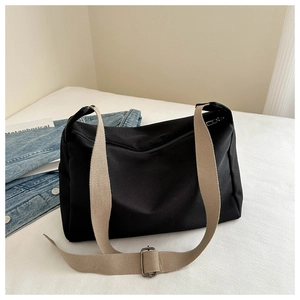Detail of a large black nylon crossbody bag with an adjustable khaki shoulder strap