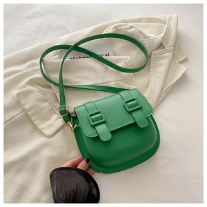 Detailed view of green saddle bag with dual matte straps and gold buckles on soft fabric
