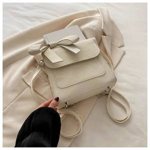 Detail of the cream textured leather backpack featuring a large bow and silver base studs