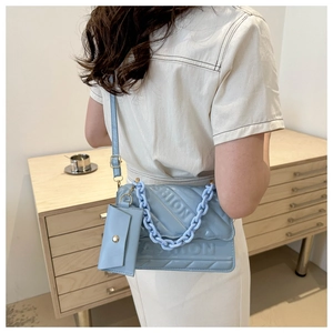 Detail of light blue quilted crossbody bag with FASHION lettering and chunky chain strap