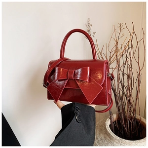 Détail d'un sac bandoulière en cuir verni rouge foncé avec un grand nœud et une poignée