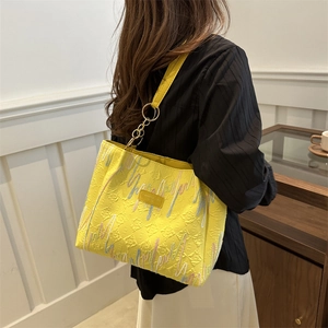Bright yellow textured tote bag with embroidery details shown on model in minimal interior