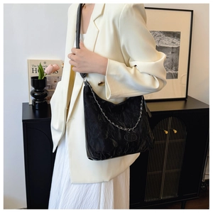 Détail du sac à bandoulière noir plissé avec chaîne argentée et veste chic