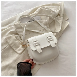 Front view of white saddle crossbody bag with dual buckles on a minimalist blazer background