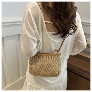 Close-up of woven straw crossbody bag with brown leather strap and knot detailing
