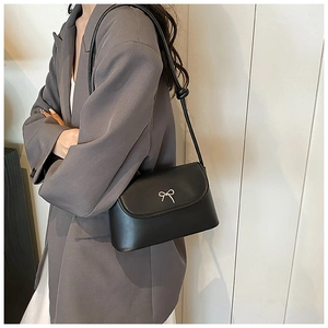 Detail of black matte shoulder bag featuring elegant silver bow buckle and slim strap