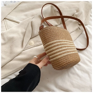 Détail d'un sac seau en paille tressée avec rayures brunes et bandoulière en cuir