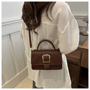Détail du sac bandoulière en cuir marron foncé avec boucle dorée portée à l'épaule