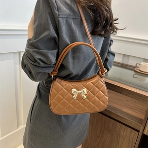 Sac bandoulière marron matelassé avec nœud doré porté par un mannequin dans un intérieur chic
