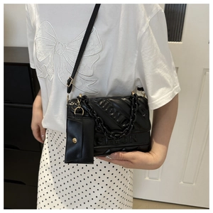 Close-up of black quilted shoulder bag featuring embossed letter and mini coin purse