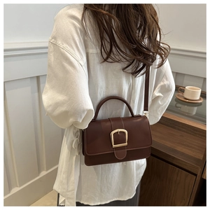 Détail d'un sac bandoulière vintage marron foncé avec boucle dorée et poignée rigide